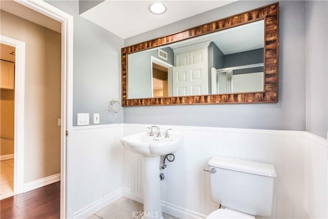 bathroom featuring toilet, a sink, wood finished floors, wainscoting, and a shower with door