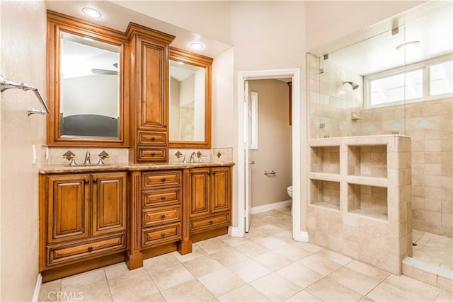 bathroom featuring toilet, double vanity, a tile shower, and a sink