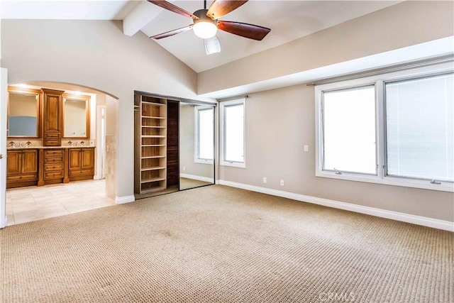 unfurnished bedroom featuring vaulted ceiling with beams, baseboards, arched walkways, and light colored carpet