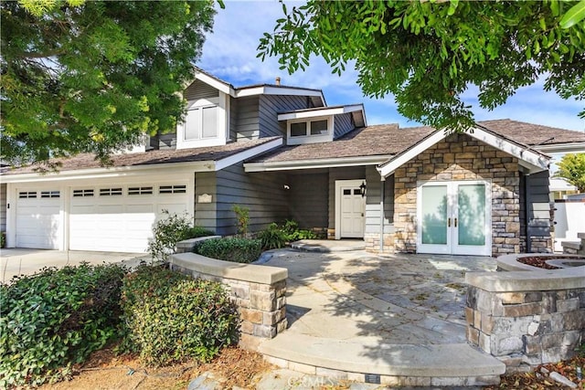 view of front of home featuring driveway, stone siding, a garage, and french doors