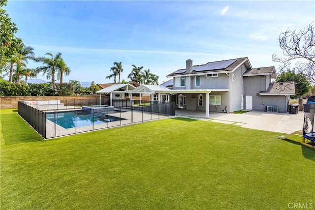 back of property featuring a yard, a fenced backyard, a patio, and solar panels