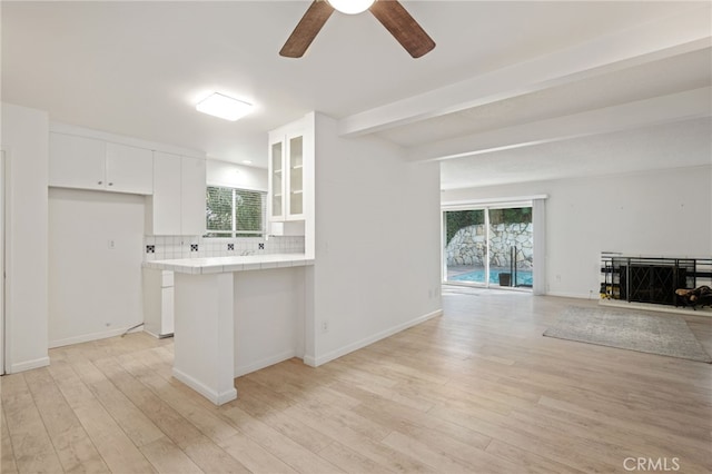 kitchen with white cabinets, light wood-type flooring, tile counters, and decorative backsplash