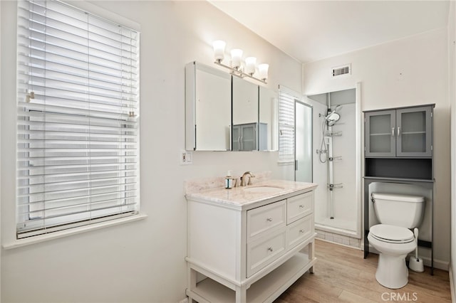 bathroom featuring hardwood / wood-style flooring, a tile shower, vanity, and toilet