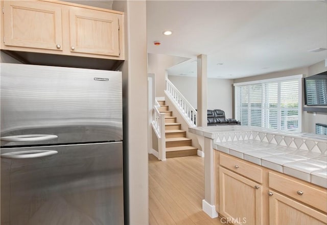 kitchen with light wood-type flooring, tile countertops, stainless steel fridge, and light brown cabinets