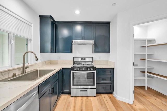 kitchen with sink, appliances with stainless steel finishes, light stone counters, and light hardwood / wood-style flooring