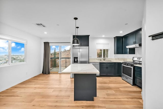 kitchen featuring stainless steel appliances, light stone countertops, light hardwood / wood-style floors, pendant lighting, and sink