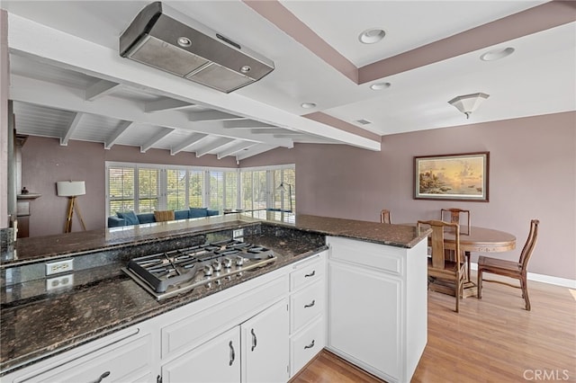 kitchen with dark stone counters, stainless steel gas cooktop, light wood-type flooring, white cabinets, and beam ceiling