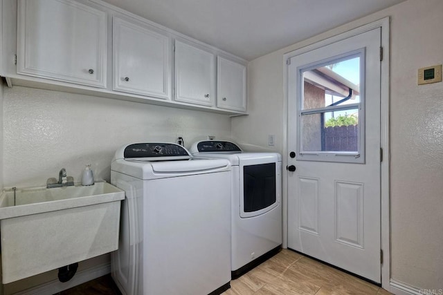 clothes washing area featuring cabinet space, separate washer and dryer, a sink, a textured wall, and light wood-type flooring