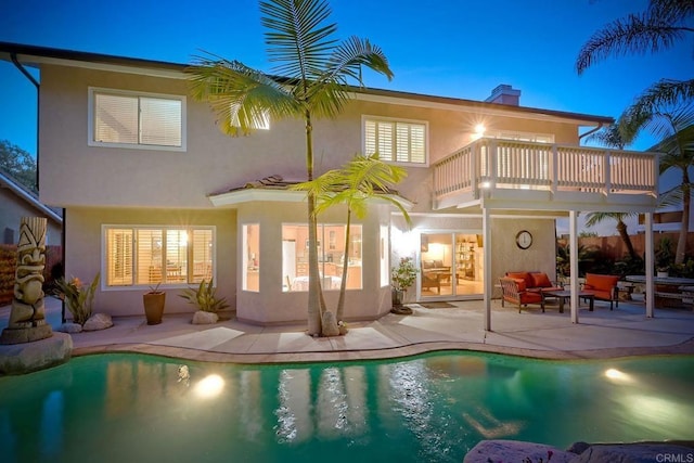 back of house featuring a balcony, stucco siding, an outdoor pool, and a patio