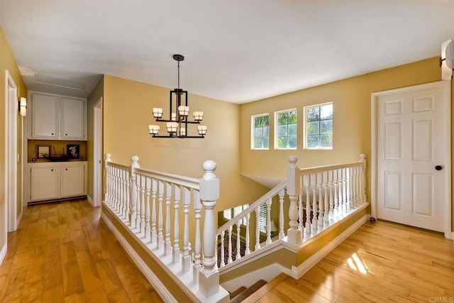 corridor with baseboards, an upstairs landing, an inviting chandelier, and light wood-style flooring