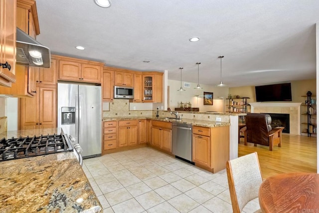 kitchen with light stone countertops, under cabinet range hood, appliances with stainless steel finishes, a peninsula, and a sink