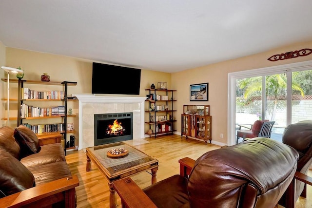 living room featuring baseboards, a tiled fireplace, and light wood finished floors