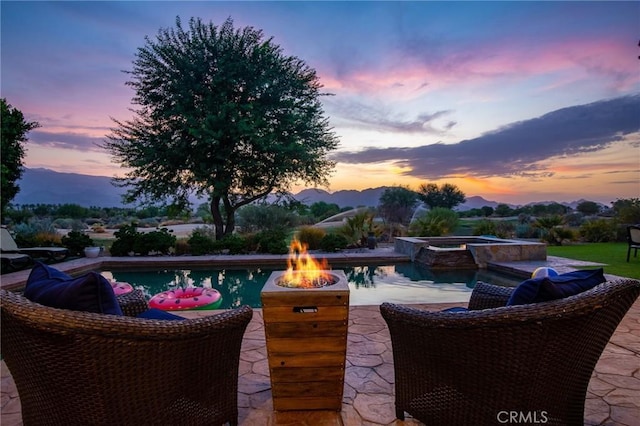 pool at dusk with an in ground hot tub, a patio area, a mountain view, and a fire pit