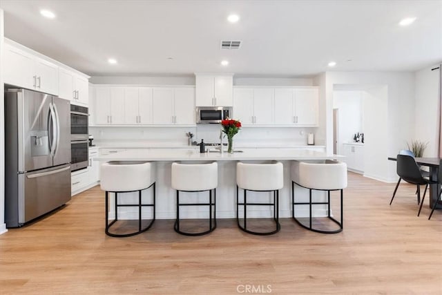 kitchen with a breakfast bar area, stainless steel appliances, light countertops, white cabinets, and visible vents