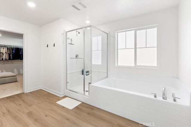 bathroom featuring a bath, a stall shower, a walk in closet, visible vents, and wood finished floors