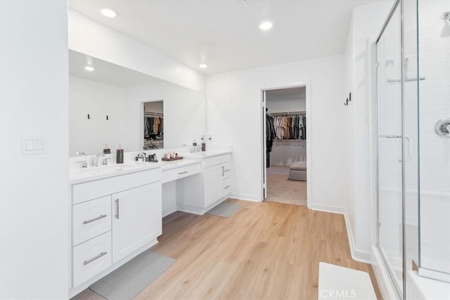bathroom featuring a walk in closet, wood finished floors, a shower stall, and vanity