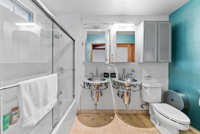 bathroom featuring enclosed tub / shower combo, a sink, toilet, and tile patterned floors