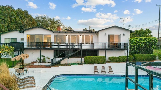 rear view of property with a sunroom, stairway, an outdoor pool, a chimney, and a patio area