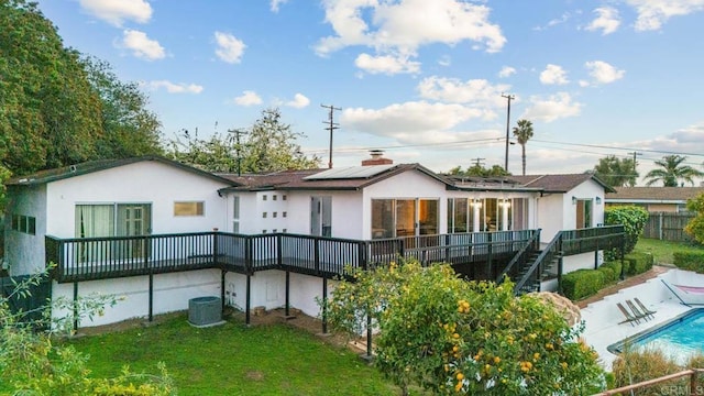 back of house featuring a lawn, stairway, an outdoor pool, and solar panels