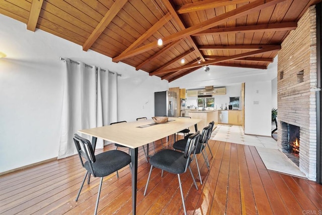 dining room featuring vaulted ceiling with beams, light wood-style flooring, a fireplace, and wood ceiling