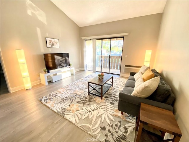 living room with lofted ceiling, a wall mounted AC, wood finished floors, and baseboards