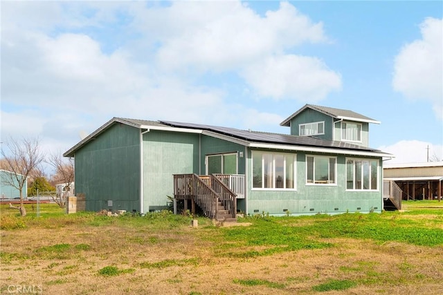 rear view of house with a lawn, roof mounted solar panels, and crawl space