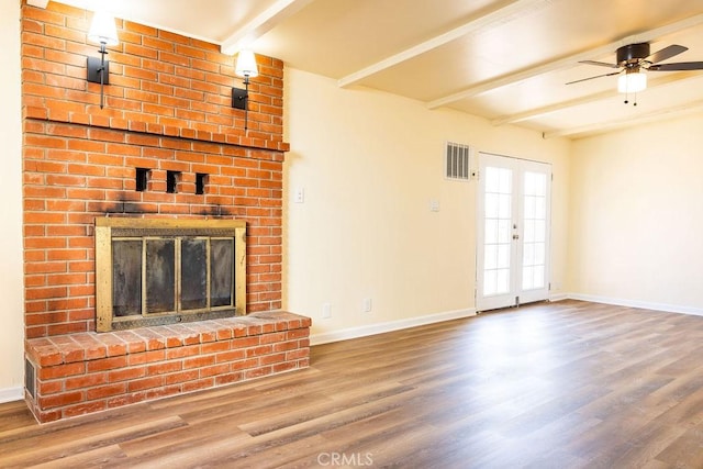 unfurnished living room featuring a brick fireplace, hardwood / wood-style flooring, beamed ceiling, and ceiling fan