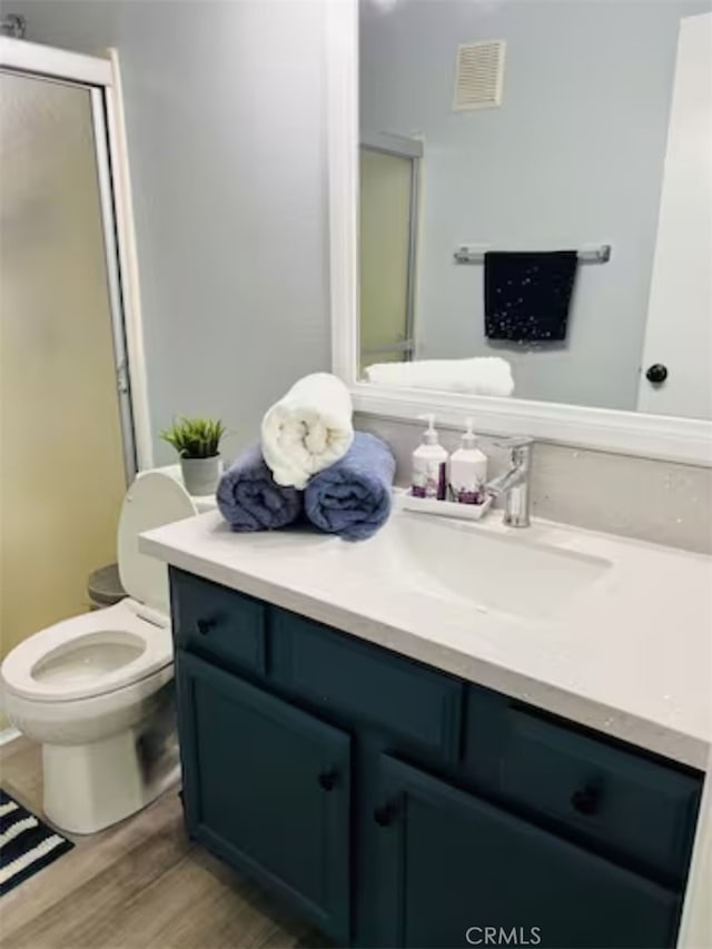 bathroom featuring hardwood / wood-style flooring, vanity, toilet, and a shower with door