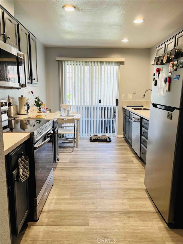 kitchen with sink, light hardwood / wood-style floors, a textured ceiling, and appliances with stainless steel finishes