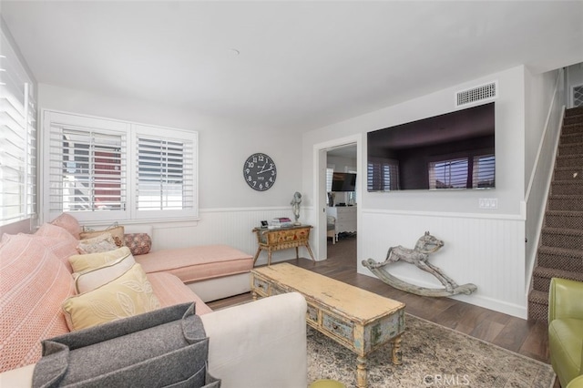 living area with visible vents, a wainscoted wall, stairway, and wood finished floors