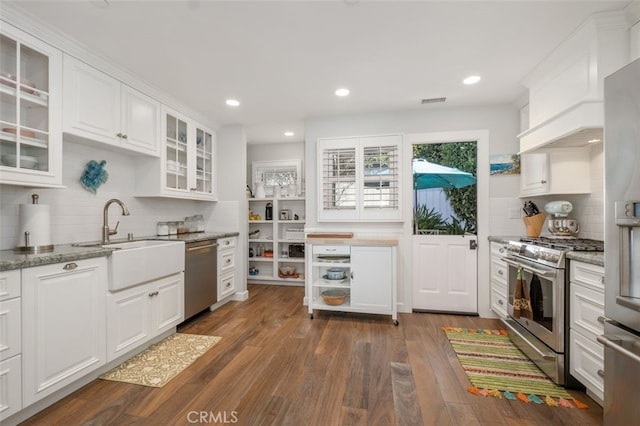 kitchen with glass insert cabinets, appliances with stainless steel finishes, dark wood-type flooring, white cabinetry, and a sink