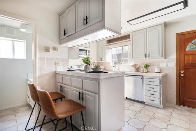 kitchen featuring tile walls, sink, stainless steel dishwasher, and a kitchen breakfast bar