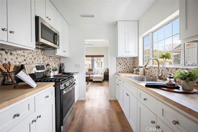 kitchen featuring sink, tasteful backsplash, hardwood / wood-style flooring, stainless steel appliances, and white cabinets