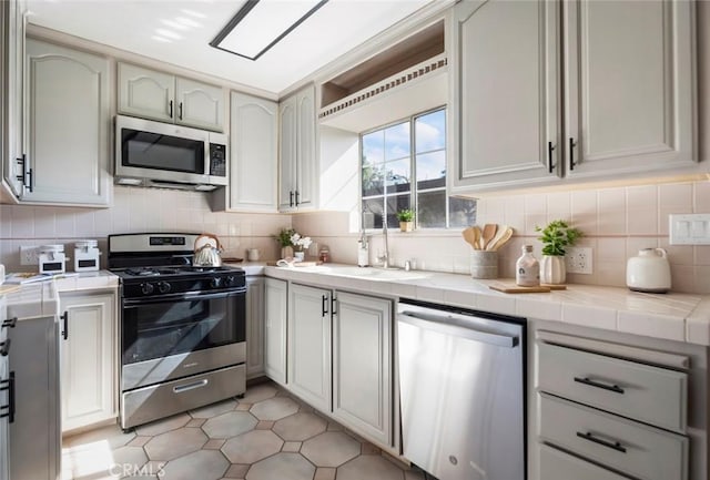 kitchen with appliances with stainless steel finishes, sink, tile countertops, and backsplash