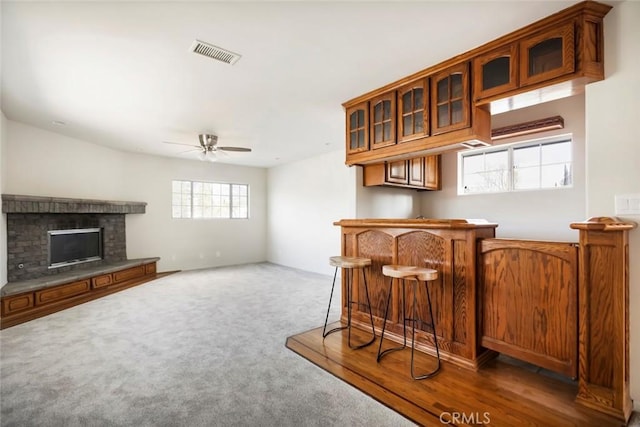 kitchen with dark colored carpet, a kitchen bar, ceiling fan, and a fireplace