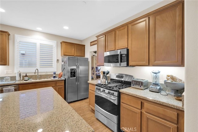 kitchen featuring sink, light hardwood / wood-style flooring, light stone countertops, and appliances with stainless steel finishes