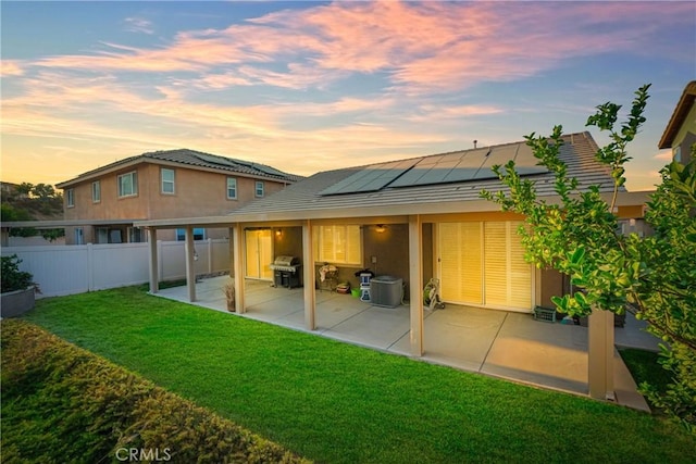 back house at dusk featuring cooling unit, a yard, a patio area, and solar panels