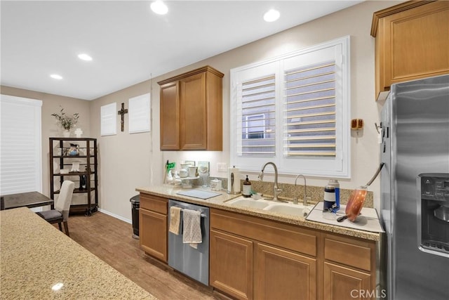 kitchen with stainless steel appliances, light stone countertops, sink, and light hardwood / wood-style flooring