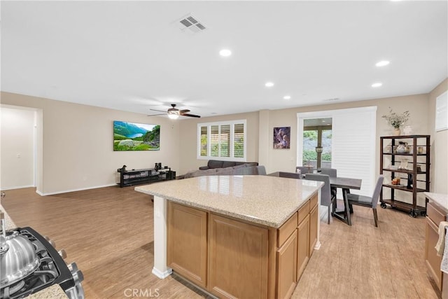 kitchen featuring light stone countertops, a center island, ceiling fan, and light hardwood / wood-style flooring