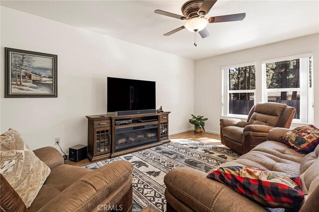 living area featuring a glass covered fireplace, wood finished floors, baseboards, and ceiling fan