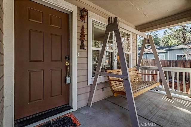 view of exterior entry featuring a porch and fence