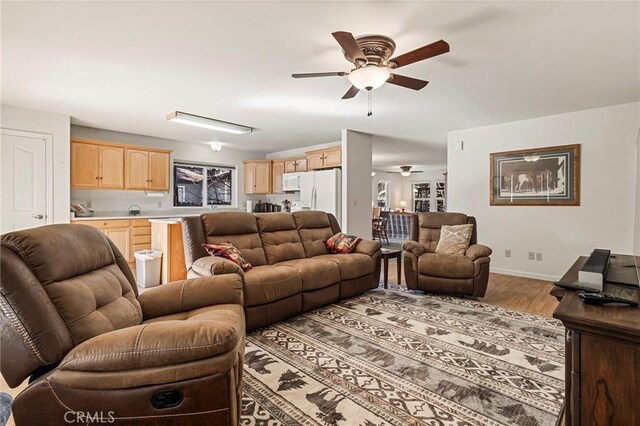 living area featuring light wood finished floors, ceiling fan, and baseboards