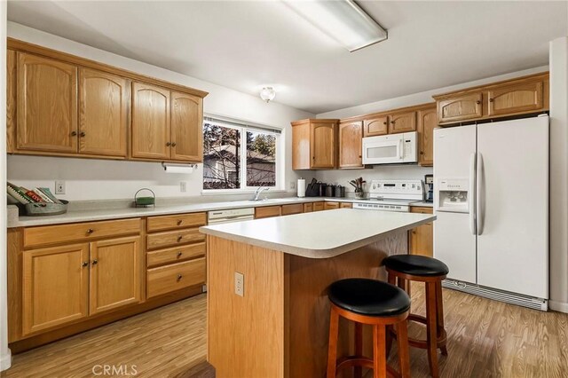 kitchen featuring light wood-type flooring, a kitchen bar, a kitchen island, white appliances, and light countertops