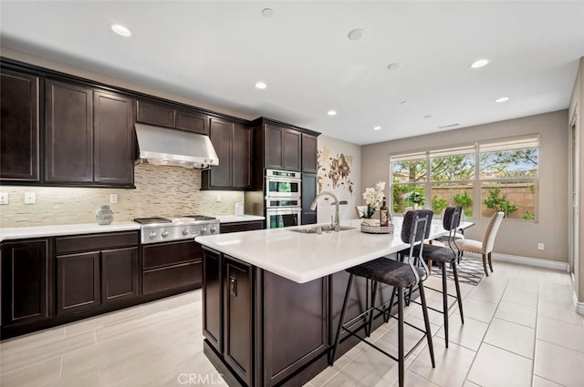 kitchen featuring tasteful backsplash, stainless steel appliances, light countertops, under cabinet range hood, and a sink