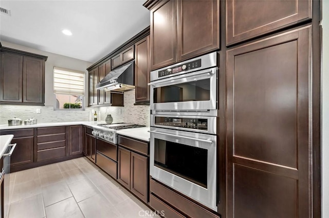 kitchen featuring stainless steel appliances, tasteful backsplash, light countertops, dark brown cabinetry, and extractor fan