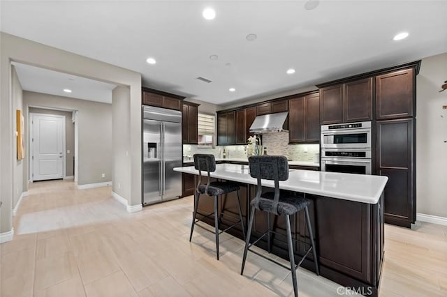 kitchen featuring dark brown cabinetry, under cabinet range hood, stainless steel appliances, a kitchen island, and light countertops