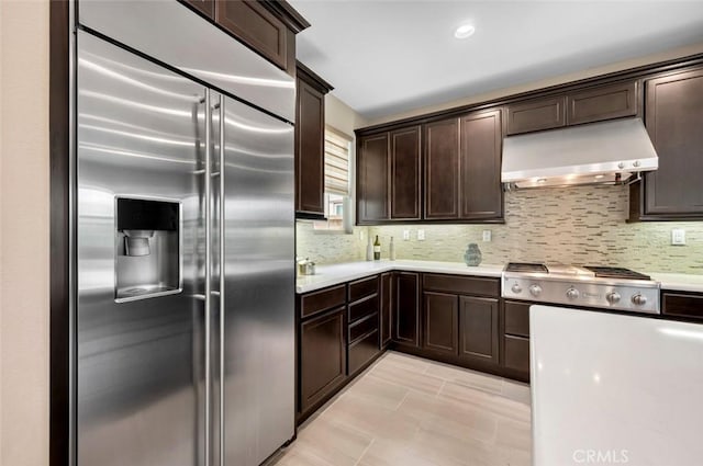 kitchen featuring tasteful backsplash, stainless steel appliances, dark brown cabinets, light countertops, and under cabinet range hood