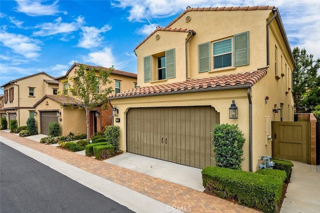 mediterranean / spanish-style house featuring a garage, a tiled roof, decorative driveway, and stucco siding