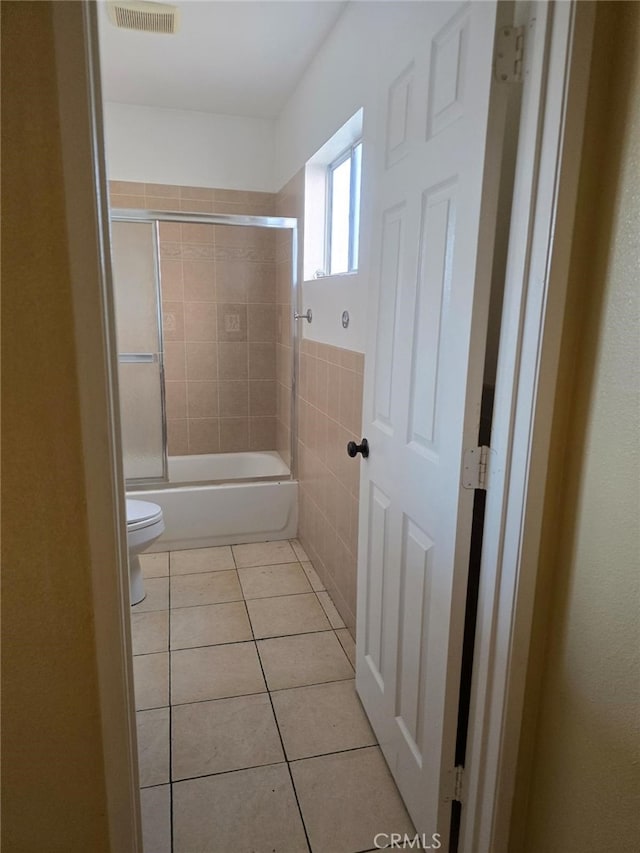 bathroom with tile patterned flooring, enclosed tub / shower combo, tile walls, and toilet