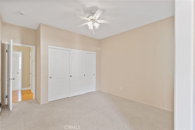 unfurnished bedroom featuring ceiling fan, a closet, and light colored carpet